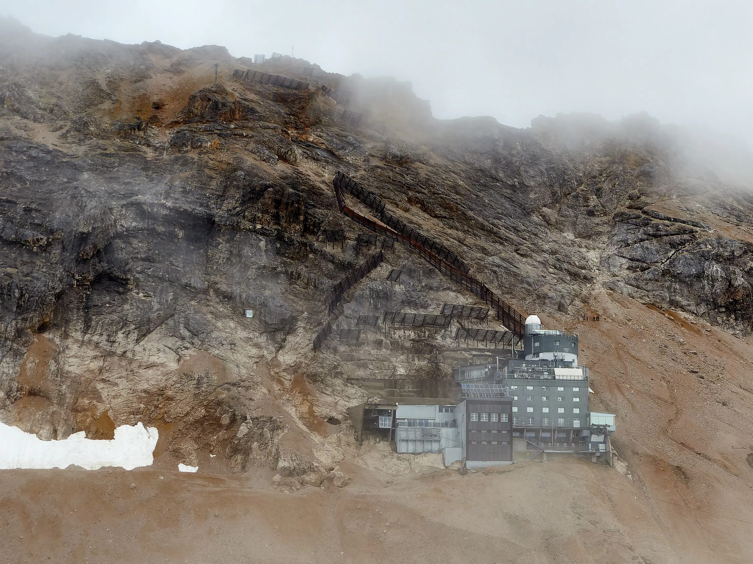 Bergstation mit Kuppel und Lawinenverbauungen an einem nebelverhangenen Schutthang im Hochgebirge