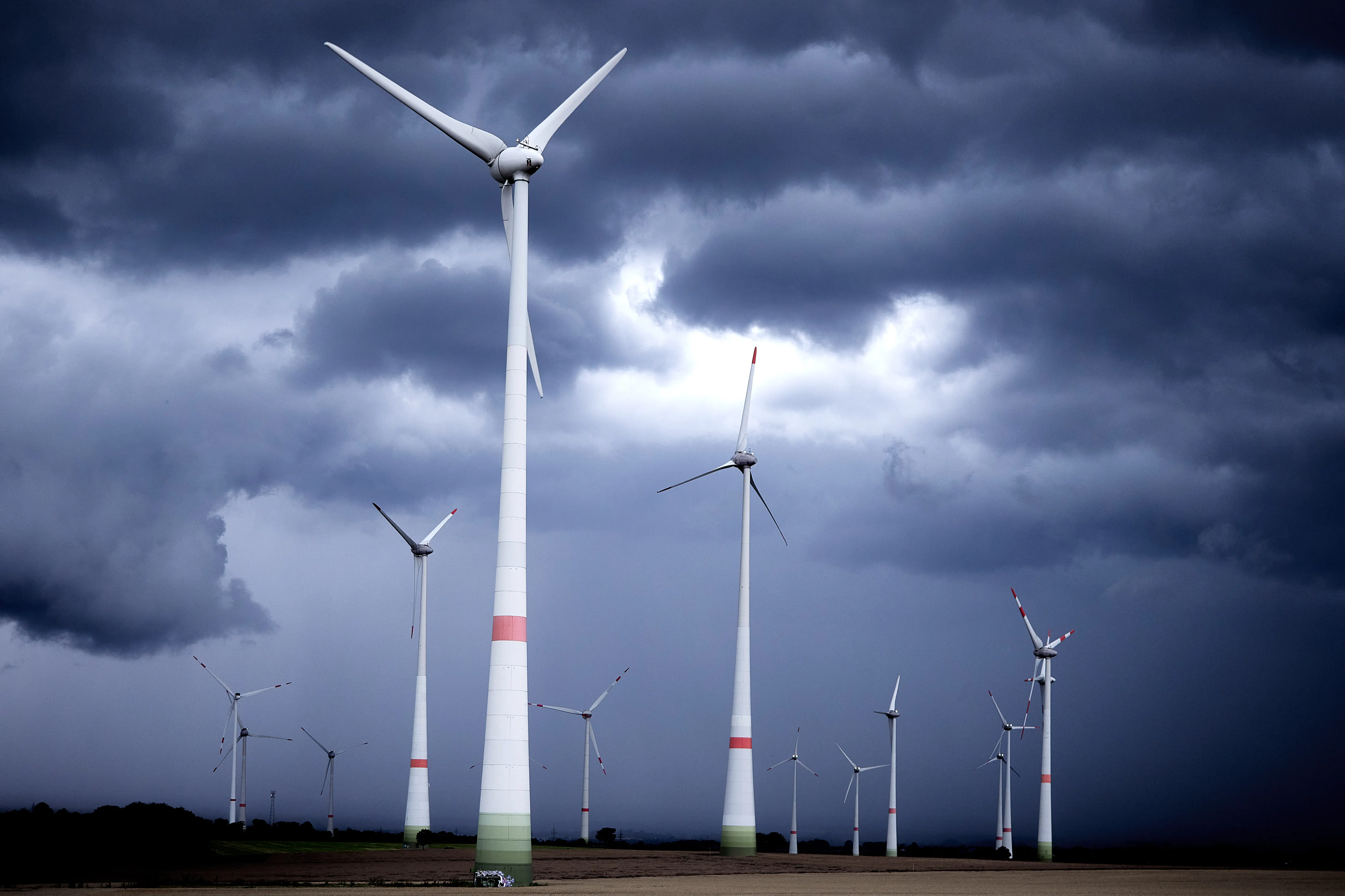 Windräder auf einem abgeernteten Feld vor einer dunklen, aufziehenden Gewitterfront