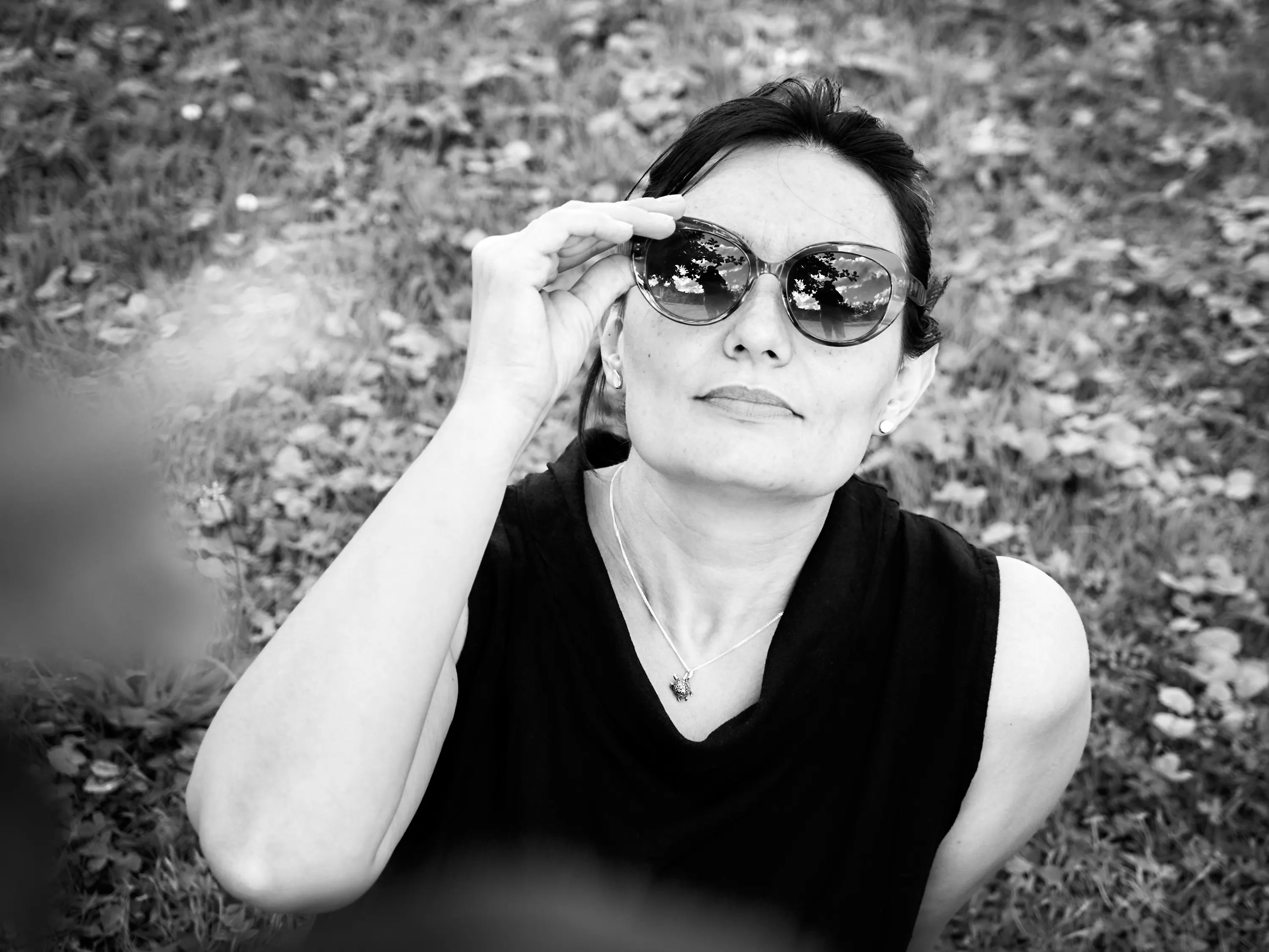 Schwarzweiß-Porträt einer Frau, die im Gras liegt und ihre Sonnenbrille anhebt