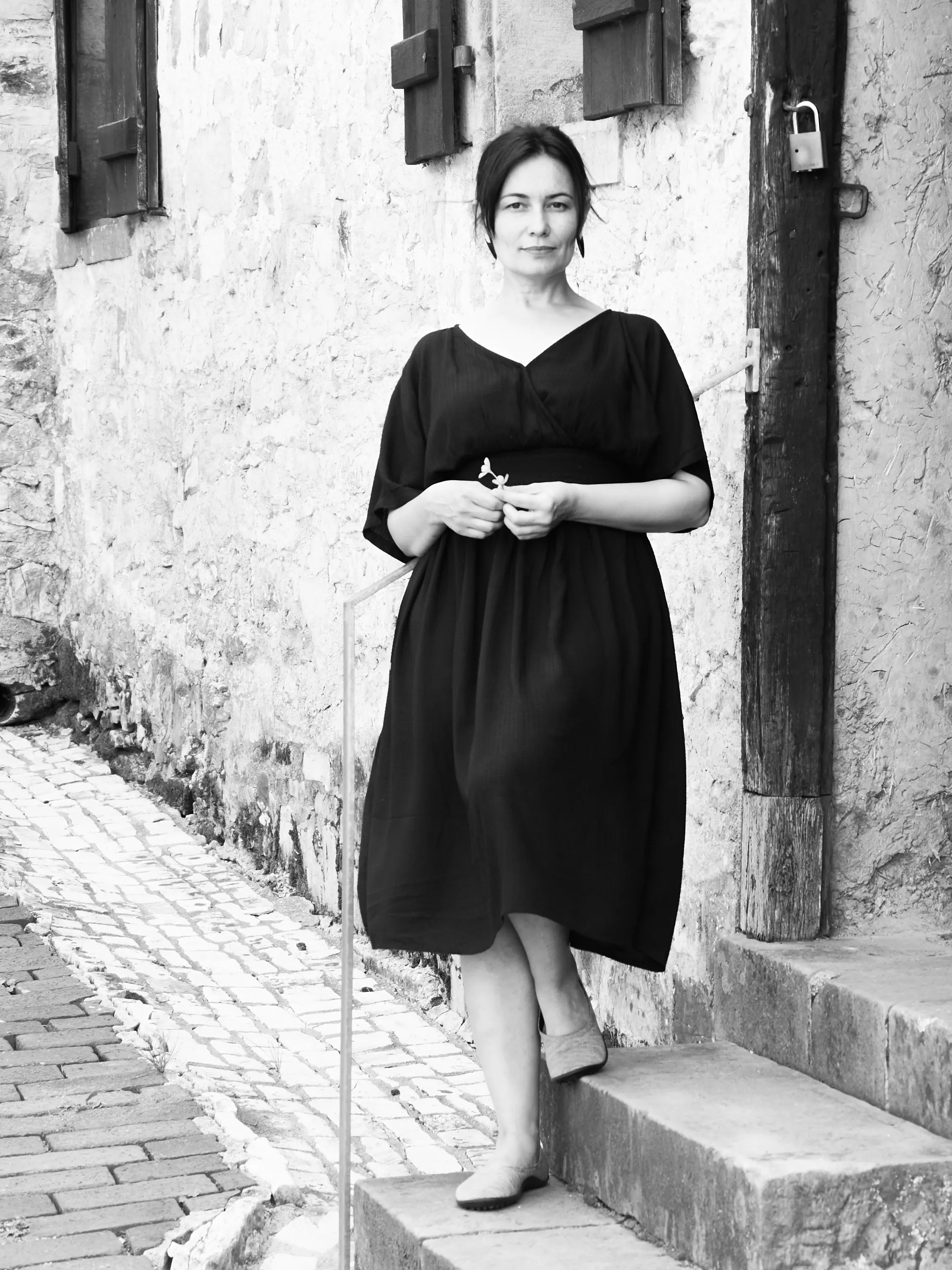 Schwarzweiß-Ganzkörperporträt einer Frau im schwarzen Kleid auf einer Steintreppe in einer alten Gasse